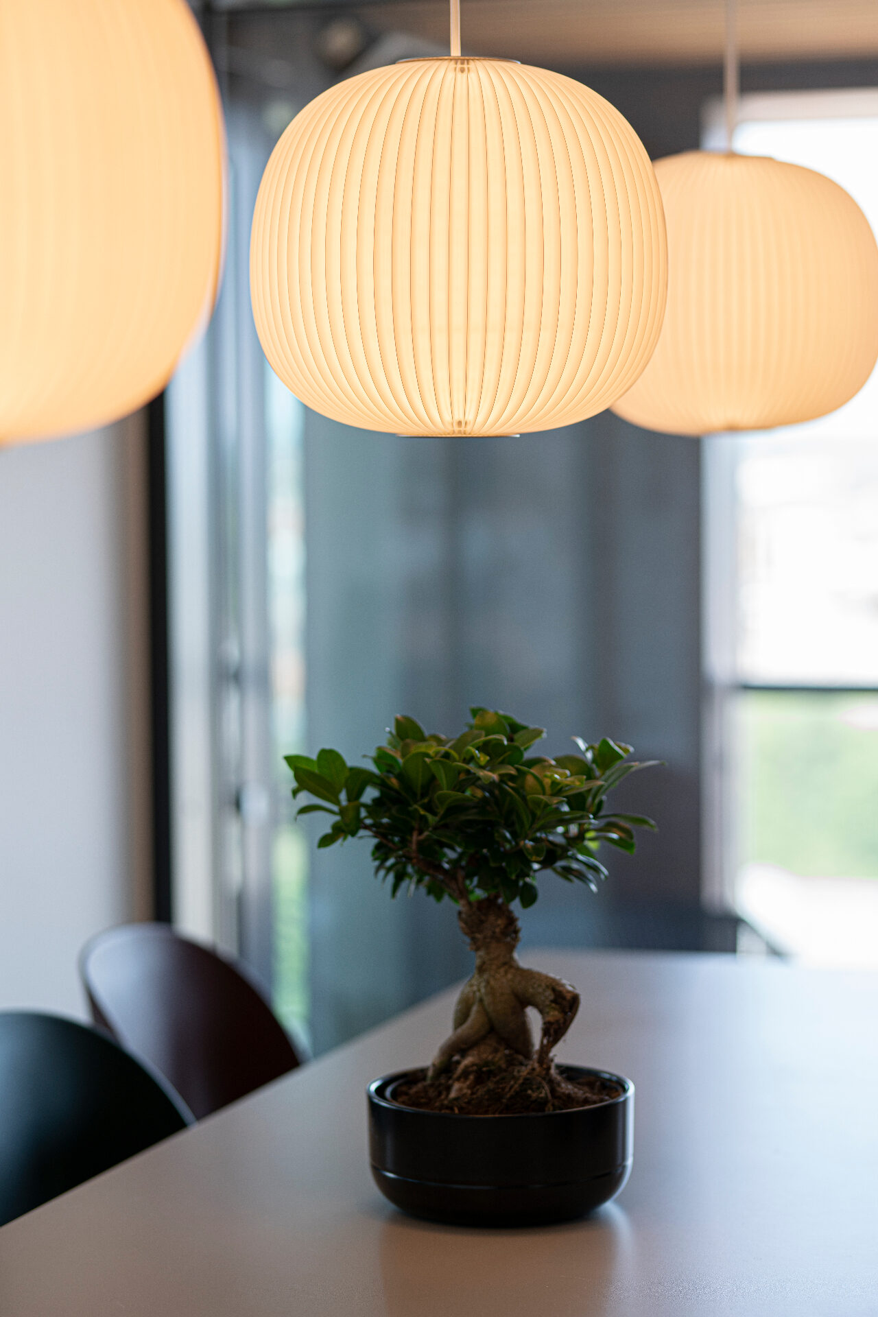 Mødebord hos PH Elteknik med varme pendellamper og en bonsai i forgrunden.