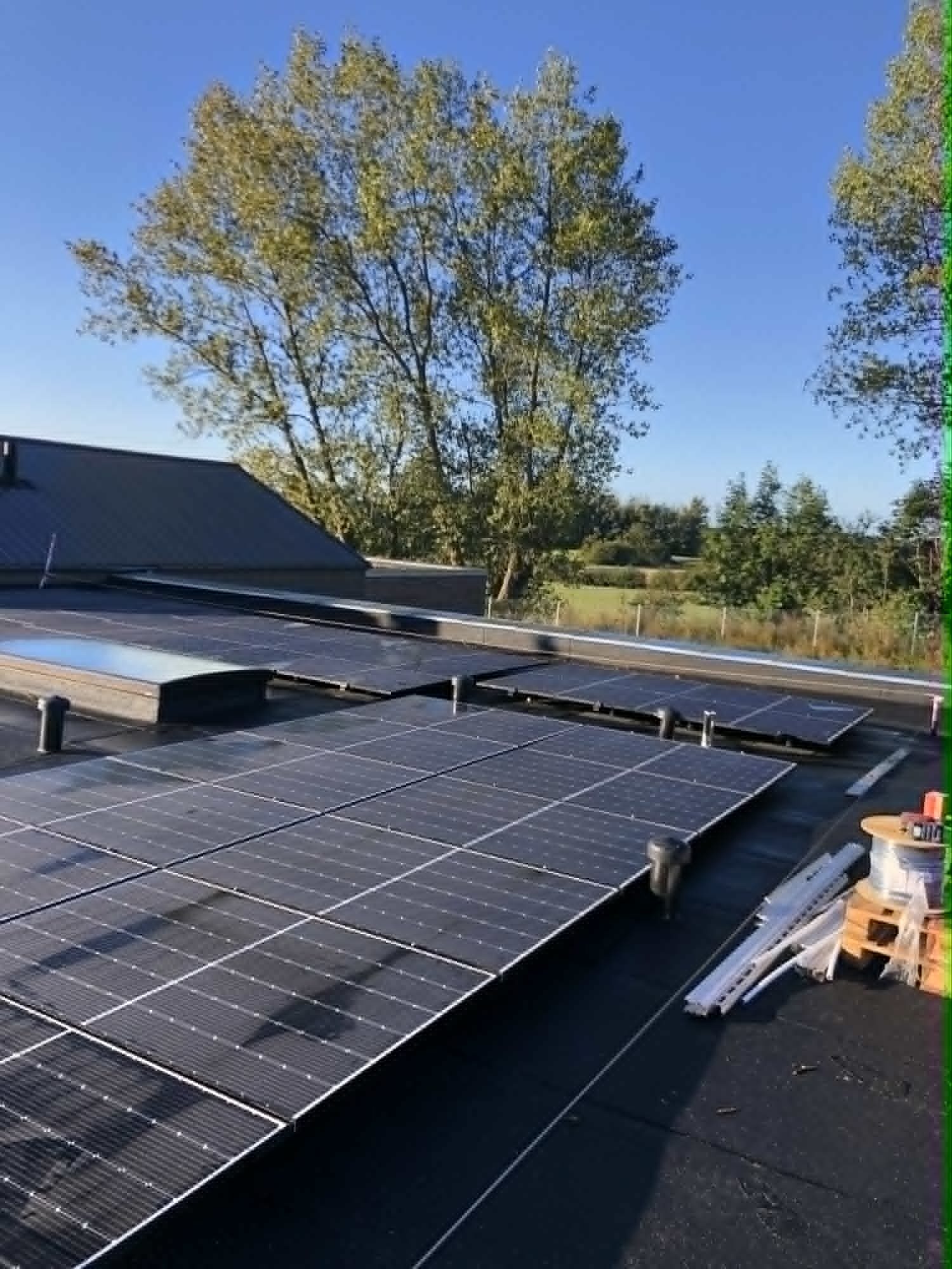 Solcelleanlæg installeret af PH Elteknik på fladt tag med åbent landskab i baggrunden.