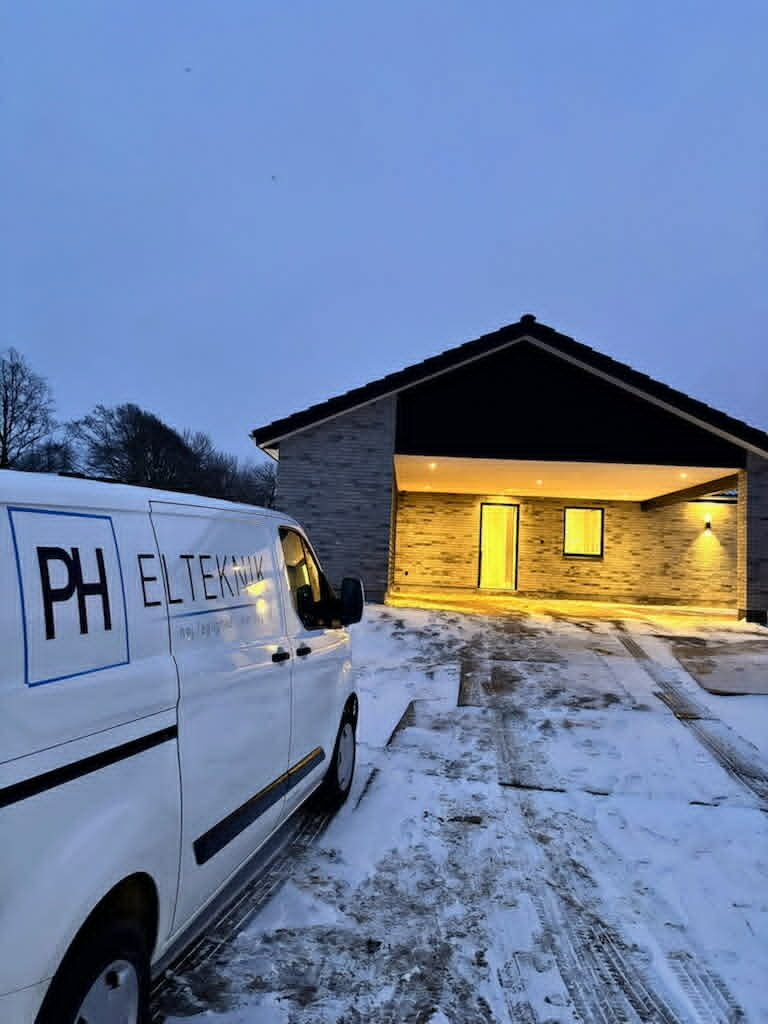 PH Elteknik servicebil ved nyopført bolig med tændt udebelysning i vintervejr.